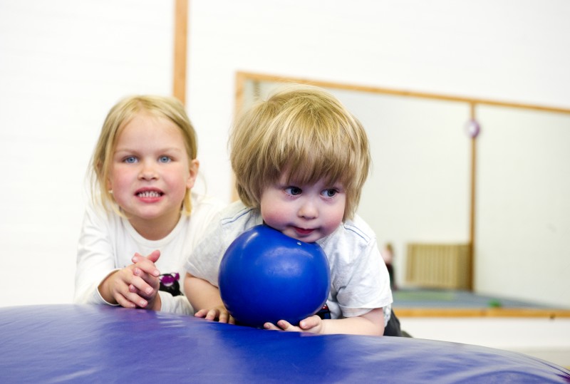 Zwei Kinder in der Turnhalle liegen auf einer Matte und halten einen Ball in der Hand.