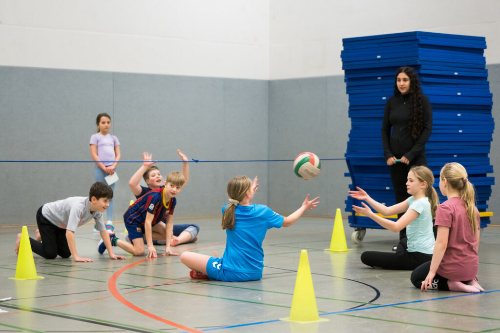 Kinder spielen in einer Turnhalle mit einem Volleyball.