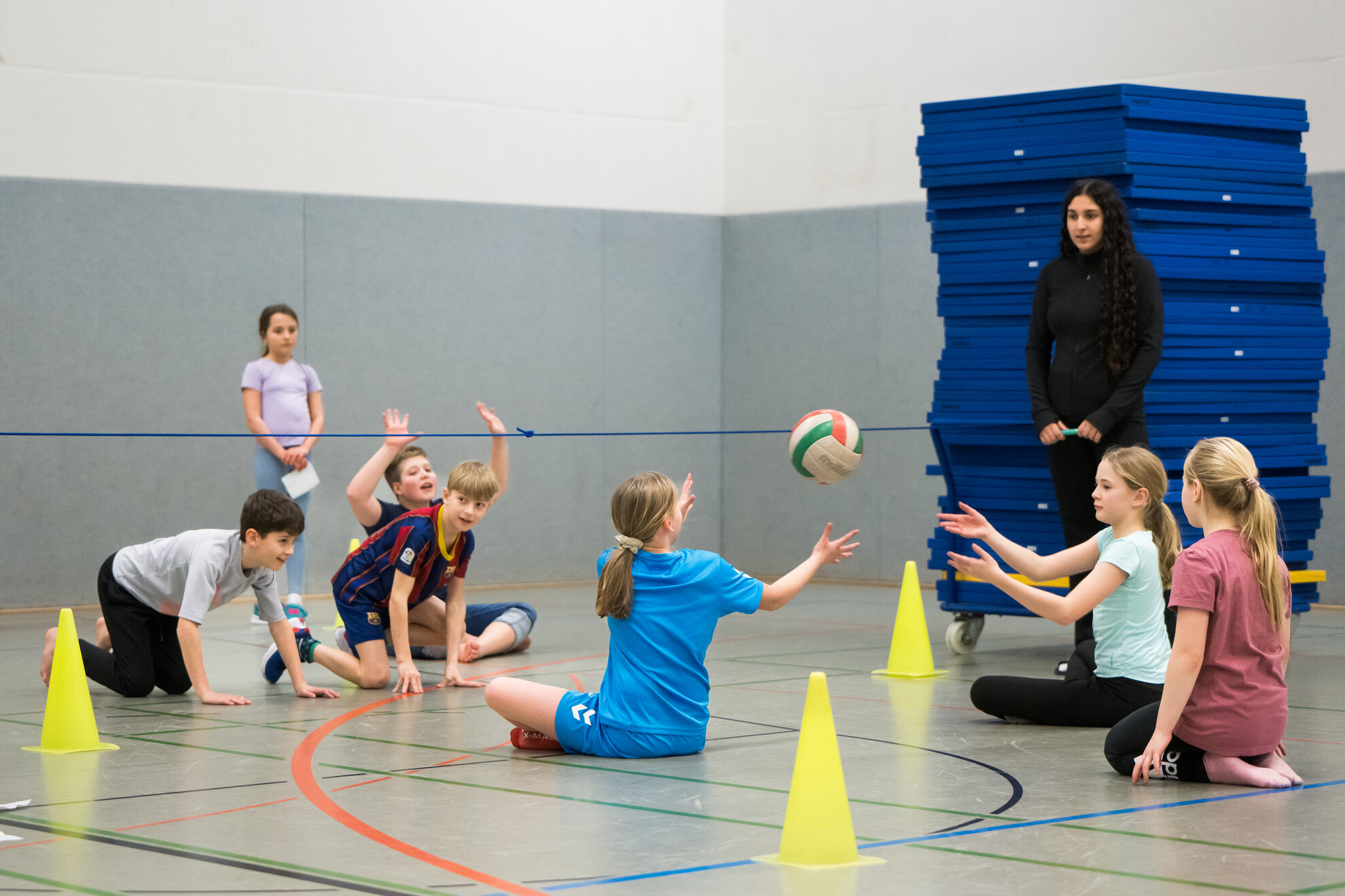 Kinder spielen in einer Turnhalle mit einem Volleyball.