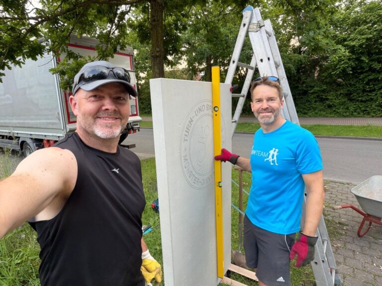 Tim Güss, Abteilungsleiter Tennis, und Andreas Brünen befestigen die neue Stele an der Einfahrt zur Tennisanlage des TSC.