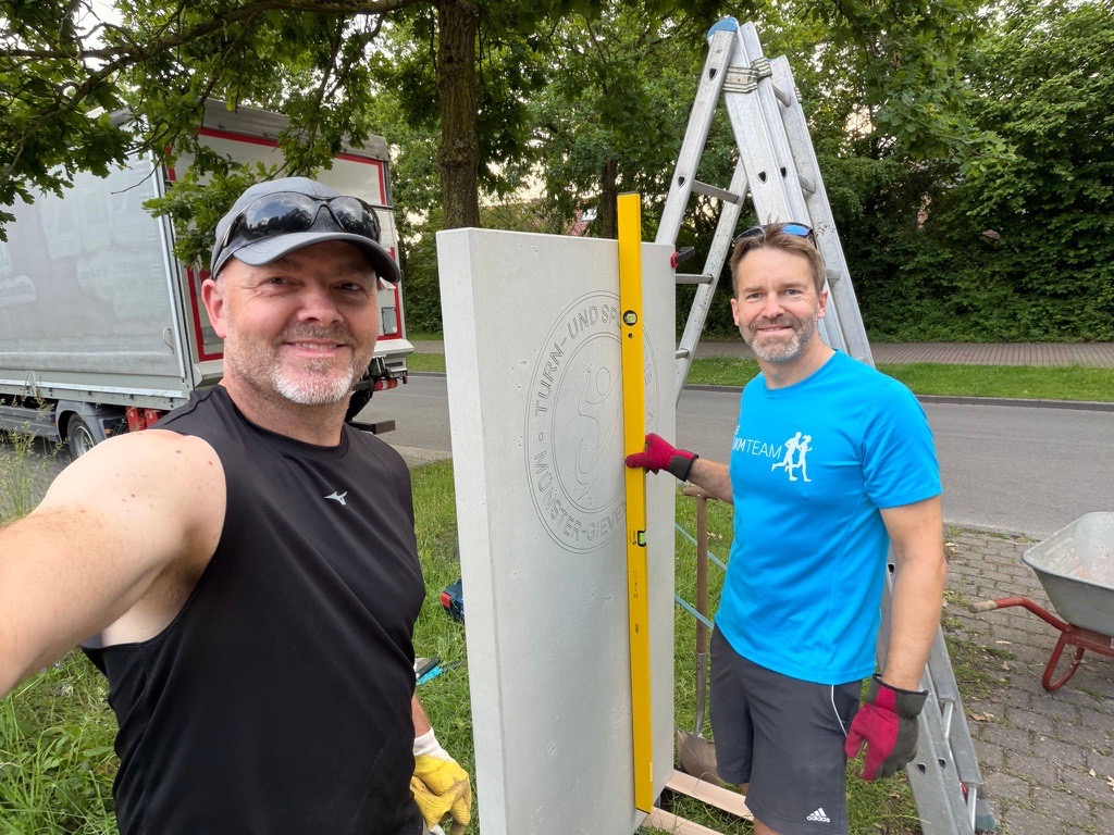 Tim Güss, Abteilungsleiter Tennis, und Andreas Brünen befestigen die neue Stele an der Einfahrt zur Tennisanlage des TSC.