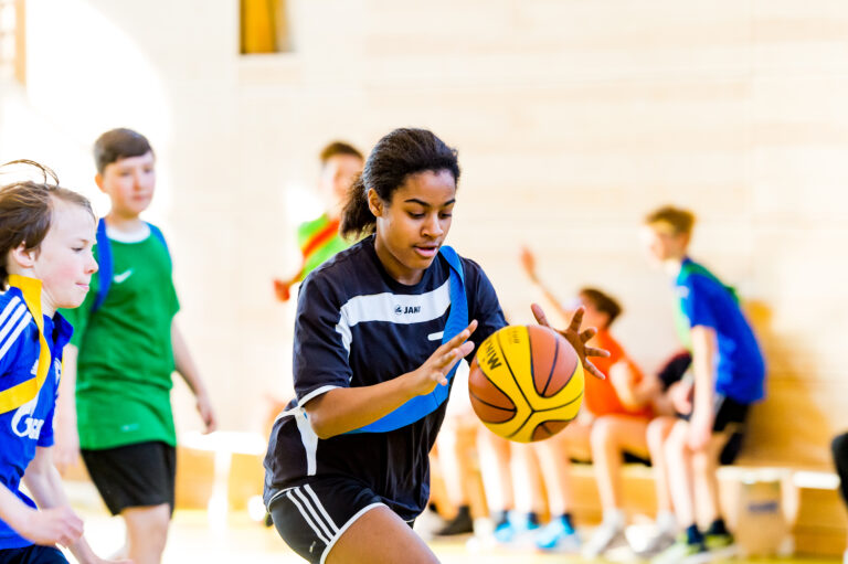 Kinder spielen Basketball in der Sporthalle.